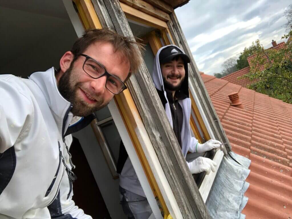 Zwei Personen auf einer Baustelle lehnen aus einem Fenster